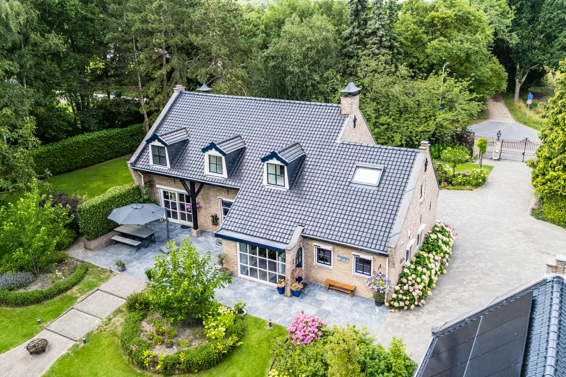 Dronefoto van een vrijstaande woning met tuin, oprit en bomen