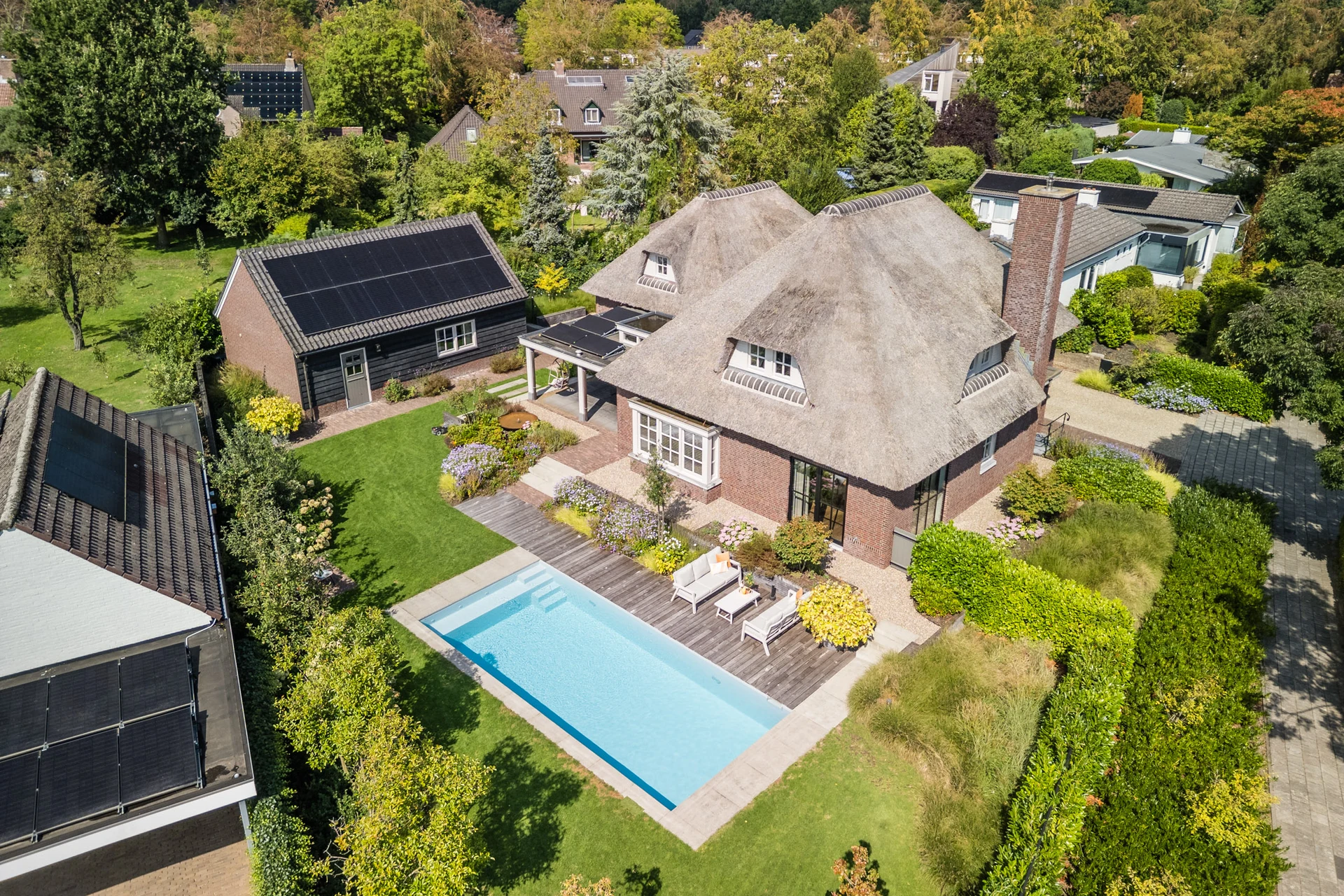 Dronefoto van een vrijstaande woning met rieten dak, tuin en zwembad
